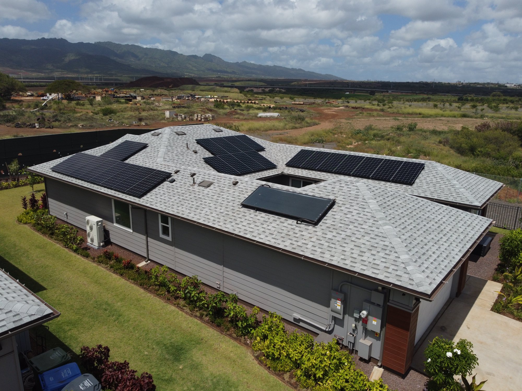 Aerial view of a single-story home with rooftop solar panels and the Waianae mountains behind